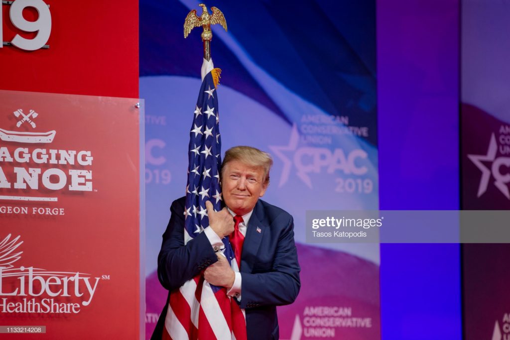 Donald John Trump, of Trump University, hugs the U.S. flag, at the Conservative Political Action Conference of 2019, National Harbor, Maryland, Saturday, 2 March 2019. (Photographer Tasos Katopodis / Getty Image News via Getty Images.)